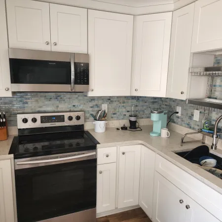 Modern white kitchen with stainless steel stove, microwave, blue tile backsplash, and dish-filled sink.