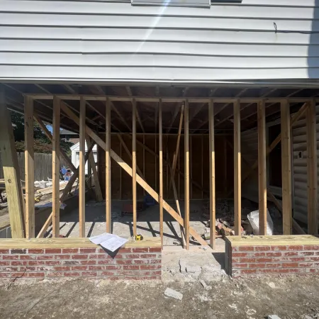 Construction site showing wooden framing and brick foundation of a building addition under a white house.