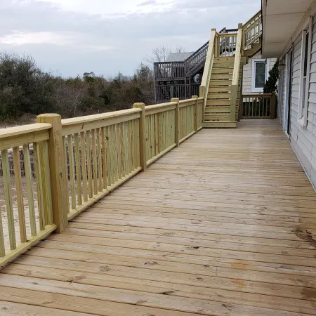 Spacious wooden deck attached to a house with stair access and natural landscape in the background