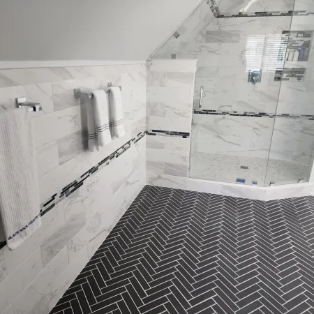 Modern bathroom with black herringbone floor tiles and white marble wall tiles with accent strip and glass shower.