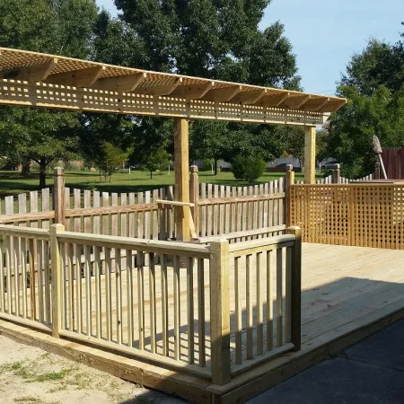 Wooden backyard deck with pergola, fencing, barbecue grill, and lattice privacy screen under clear sky.