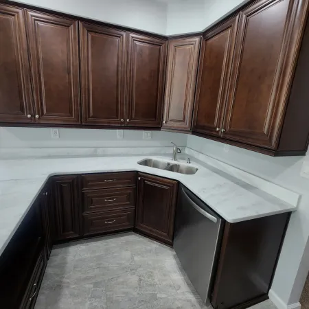 Modern kitchen with dark wood cabinets, white marble countertops, stainless steel dishwasher, and sink.