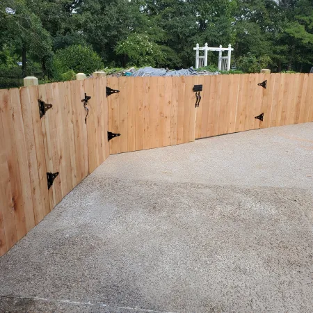 Newly installed wooden privacy fence with black metal hinges enclosing a driveway and backyard area.