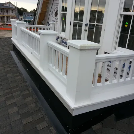 Close-up of a white wooden railing on a rooftop balcony with shingled roof and houses in the background.