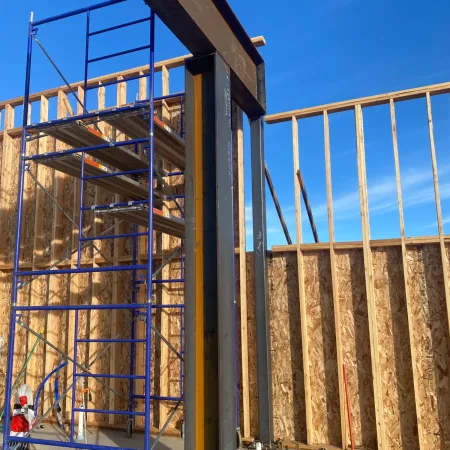 Blue metal scaffolding inside a building under construction with wooden framing and clear blue sky.
