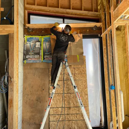 Construction worker welding inside a wooden building frame with tools and materials nearby