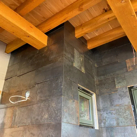 Wooden beams and dark tile wall with small window in a rustic interior under construction.