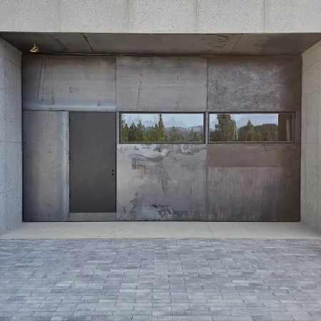 Modern concrete and metal structure with a dark door and reflective horizontal windows showing trees and mountains.