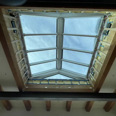 Skylight installation showing exposed wooden framing and clear sky through glass panels in ceiling.