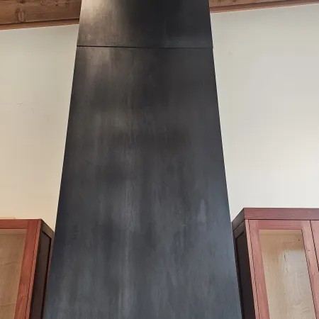 Modern black metal kitchen range hood with wooden cabinets and marble backsplash under recessed ceiling lights