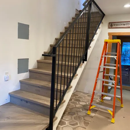 Modern wooden staircase with black metal railing and an orange ladder nearby in a home under renovation.