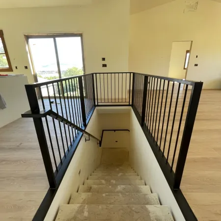 Modern staircase with black metal railing and light wood flooring in a bright, unfinished interior space.