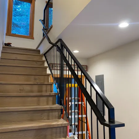 Modern wooden staircase with black metal railing and bright interior lighting in a residential home.
