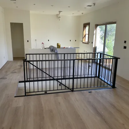 Modern open interior with light wood floors, white walls, black metal staircase railing, and large windows