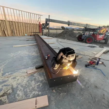 Worker welding a large steel beam inside a construction site during sunset with equipment in the background