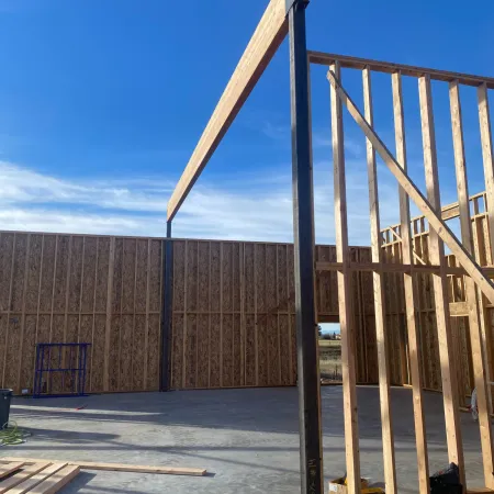 Wooden framing and steel beams on concrete foundation under clear blue sky at construction site.