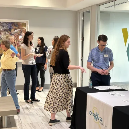 People networking and talking at an indoor professional event with a Discover Your Future table.