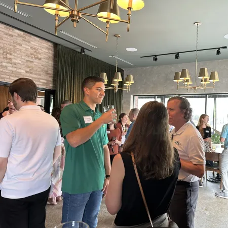 People networking and socializing in a modern, well-lit room with large windows and chandeliers.