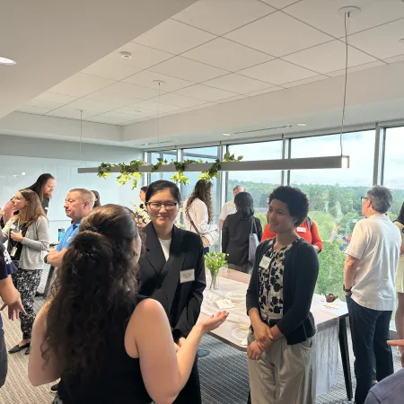 People networking and conversing at a bright indoor event with large windows and modern decor.