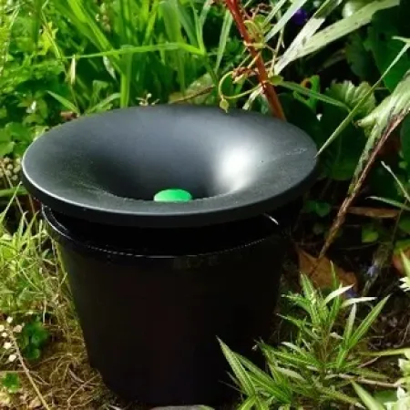 Black garden pest repeller device placed among green plants and shrubs on garden soil.