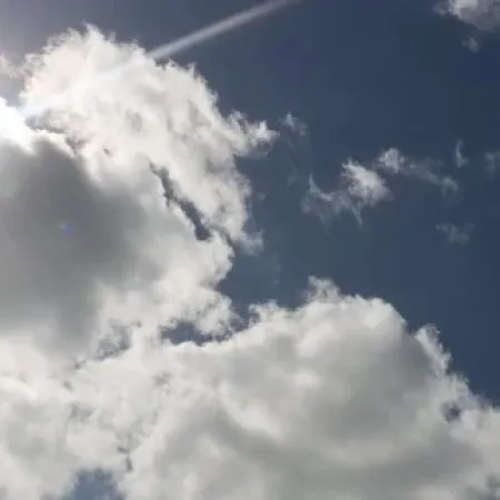 Sunlight shining through scattered fluffy white clouds in a bright blue sky.