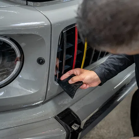 Person installing decorative trim on a gray car front grille with colorful accents around headlight area.