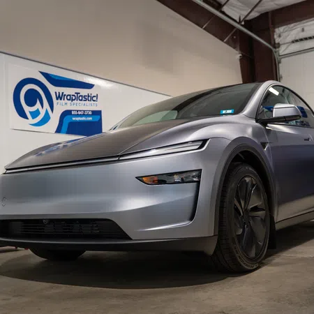 Matte gray electric car parked indoors near WrapTastic film specialist signage and equipment.