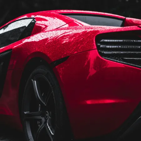 Close-up of a shiny red sports car rear with rain droplets and sleek tail light design under natural lighting.