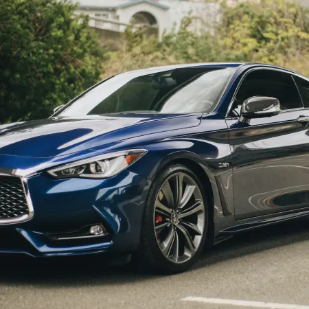 Blue Infiniti sports sedan parked outdoors near greenery and residential buildings under an overpass.