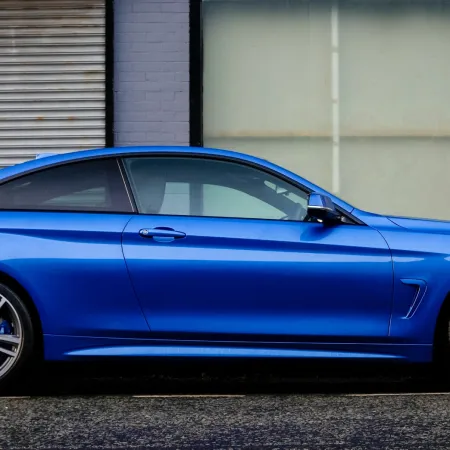 Sleek blue BMW coupe parked on street in front of gray brick building with 'Entrance' sign above door.