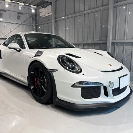 White Porsche 911 GT3 RS sports car with black rims in a bright modern garage showroom.