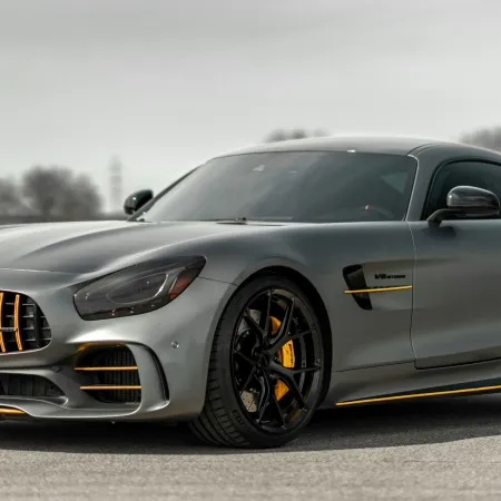 Sleek gray Mercedes AMG GT sports car with black and yellow accents parked on a road with blurred trees in background