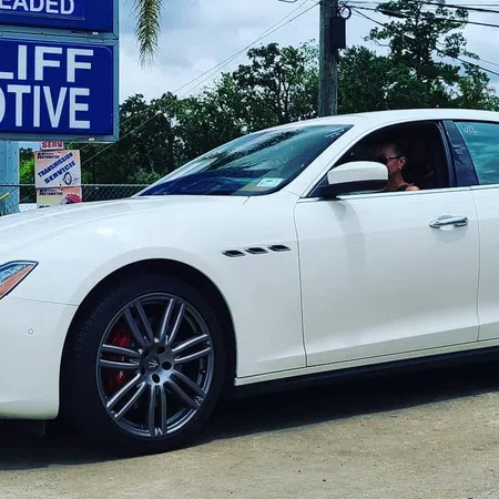 White luxury sedan parked outside Wycliff Automotive service center on a sunny day with visible signage.