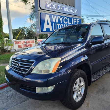 Blue Lexus GX SUV parked near Wycliff Automotive with service signs for tune-up, brakes, and oil change.