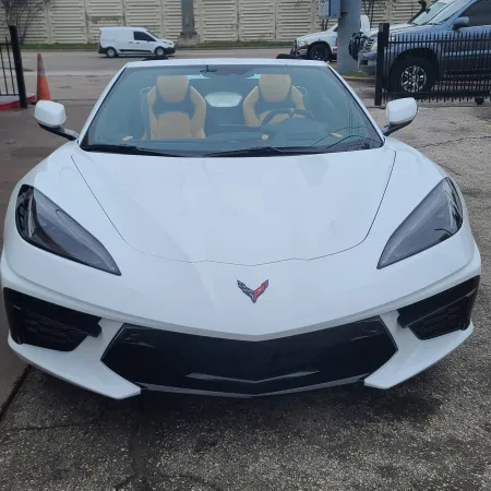 Front view of a white Corvette sports car with tan interior parked on asphalt near traffic cones.