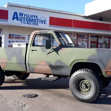 Camouflage-painted pickup truck parked outside Wycliffe Automotive with clear signage and blue sky.