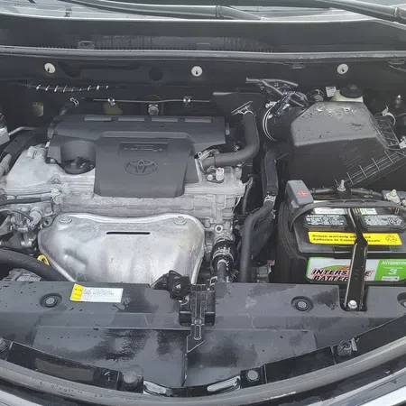 Open hood view of a Toyota car engine bay showing engine, battery, coolant reservoir, and various components.