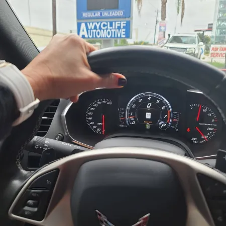 Driver's hand on Corvette steering wheel with dashboard and Wycliff Automotive sign outside the car window
