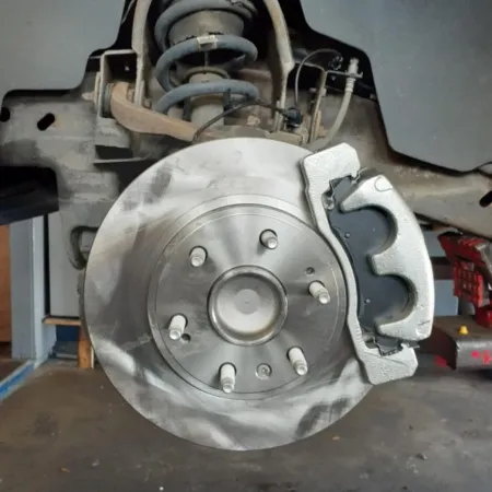Close-up of a car's brake disc and caliper assembly during maintenance or repair in a garage setting