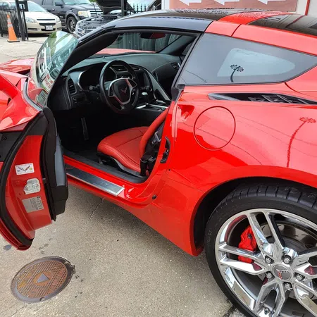 Red sports car with open door showing black and red interior, steering wheel, and shiny chrome wheels.