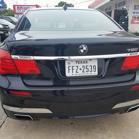 Rear view of a black BMW 750Li with Texas license plate parked outside an automotive shop.