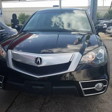 Black Acura SUV front view with chrome grille and headlights reflecting sky and surroundings.
