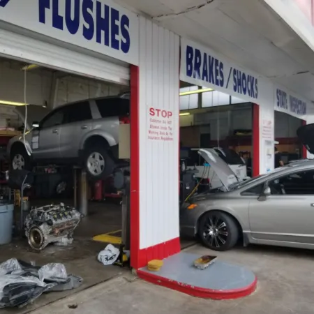 Auto repair shop with cars being serviced, one lifted and another with hood open for maintenance.