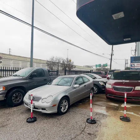 Silver Mercedes coupe parked in lot among other vehicles with red and white poles marking spaces on wet ground.
