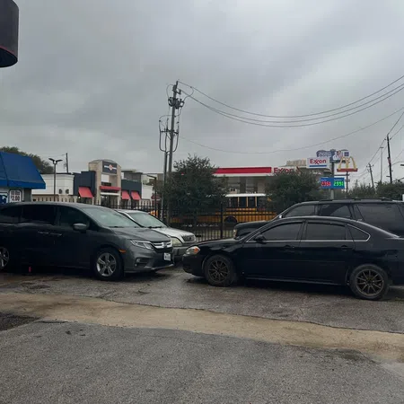 Wet parking lot with three cars, overhead power lines, a school bus, and an Exxon gas station with visible prices.