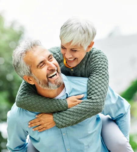 Happy mature couple outdoors enjoying piggyback ride with smiles and laughter in casual clothes.