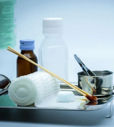 Medical tray with rolled gauze, cotton swabs, metal bowl, and medicine bottles on a white background