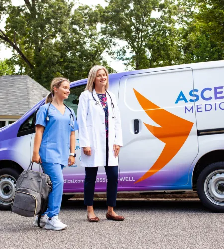 Two healthcare professionals near a branded Ascend Medical van in a residential area.