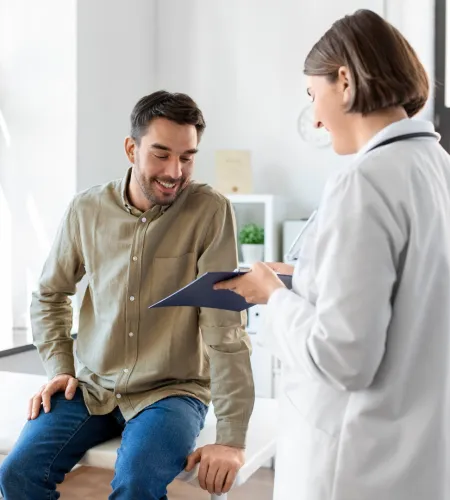 Male patient smiling while doctor discusses health information on clipboard in medical office