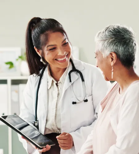 Female doctor smiling and discussing health information on tablet with older female patient in clinic